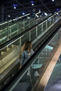 Full length of woman looking away while sitting on escalator