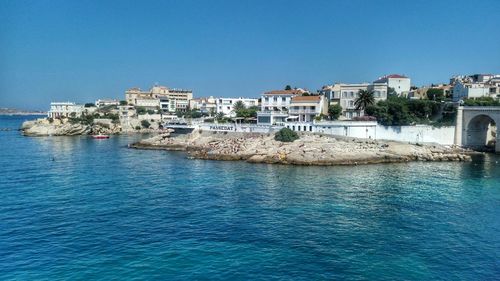 Scenic view of sea by houses against clear blue sky