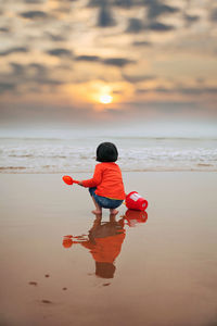 Rear view of boy on beach against sky during sunset