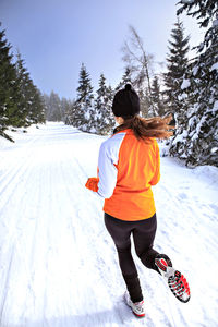 Rear view of woman running on snow covered field against sky