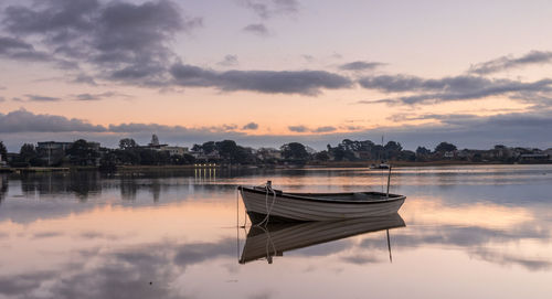 Boat moored in lake against sky during sunset