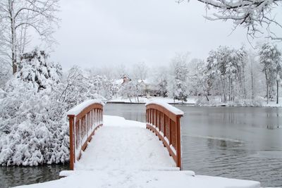 Snow covered house by lake against trees during winter