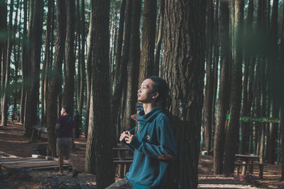 Side view of young man standing on tree trunk in forest