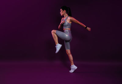 Full length of young woman exercising against black background