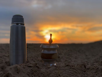 Close-up of bottle on beach against sky during sunset