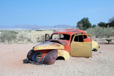 Abandoned car on landscape against clear sky