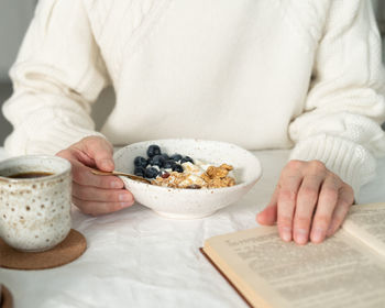 Reading book and eating healthy holiday winter breakfast with granola muesli and yogurt in bowl 