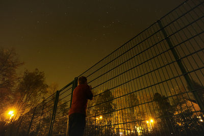 Man looking through fence against trees