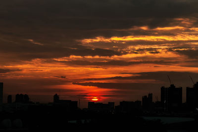 Silhouette of city against cloudy sky during sunset