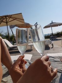 Low section of people holding drink at beach against clear sky