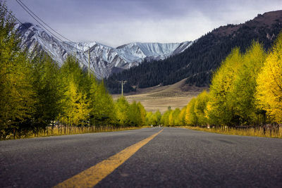 Road amidst trees and mountains against sky