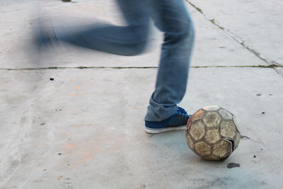 Low section of man kicking football on street