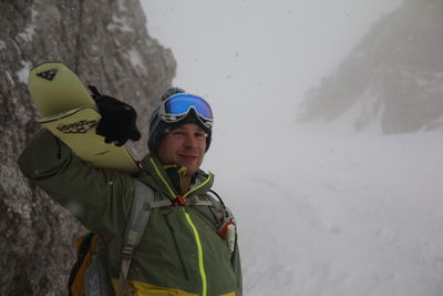 Portrait of smiling man wearing warm clothing standing on snow covered mountain