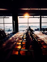 Empty chairs and tables against sky seen through glass window