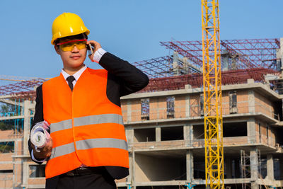 Portrait of engineer using phone at construction site against clear sky