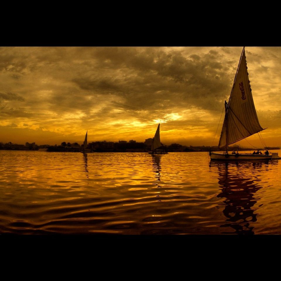 Sailboats sailing on sea against orange cloudy sky