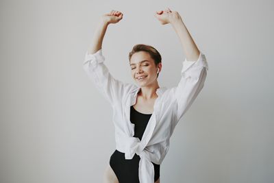 Portrait of young woman with arms raised standing against wall