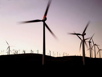 Low angle view of silhouette wind turbines on field against sky