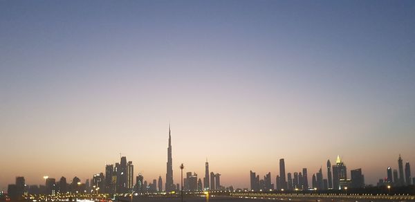 Silhouette burj khalifa in illuminated city against clear sky during sunset