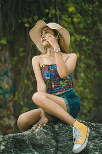 Woman wearing hat sitting on rock