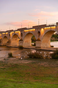 Arch bridge over river against sky during sunset