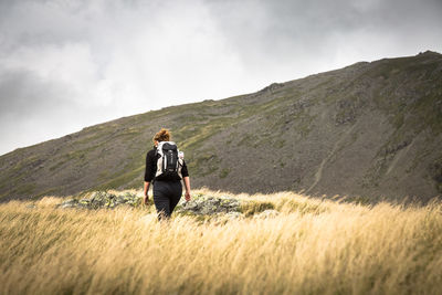 Rear view of woman standing on mountain against cloudy sky