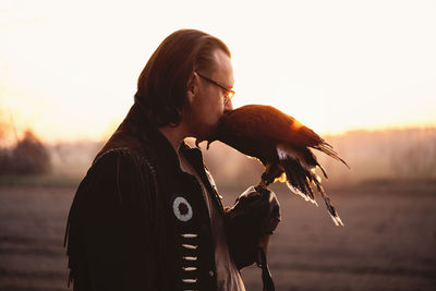 Man and wild bird over sunset sky looking on each other buzzard or eagle symbol of power, victory