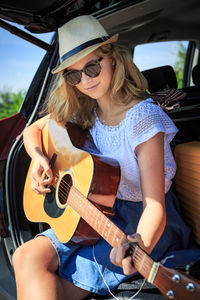 Girl playing guitar while sitting in car