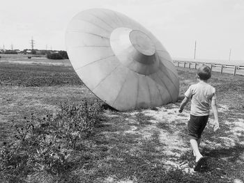 Rear view of boy walking on field towards artificial ufo