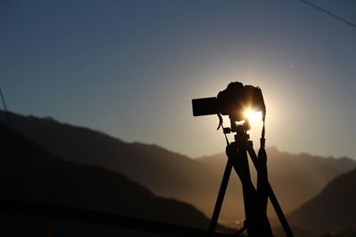 Silhouette photo camera against sky during sunset