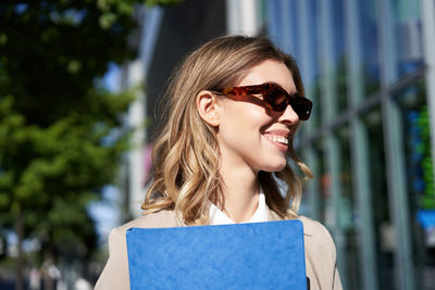 Portrait of young woman holding book while standing outdoors