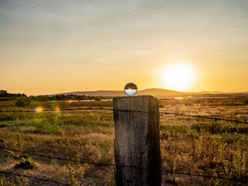 Fence on field against sky during sunset