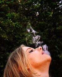 Close-up of woman emitting smoke against trees