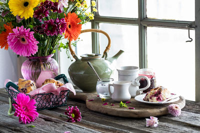 A rustic window setting of tea and scones with a vase of colourful flowers.