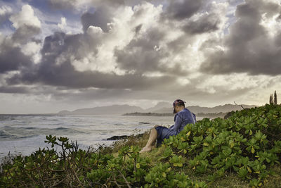 Person sitting on sea shore against sky