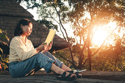 Young woman sitting on book against trees