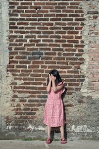 Full length of woman standing against brick wall