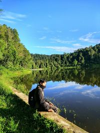 Side view of man sitting by tree against sky