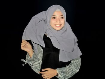 Portrait of smiling woman standing against black background