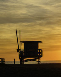 Silhouette hut on beach against sky during sunset