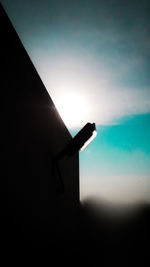 Silhouette person holding umbrella against sky during sunset