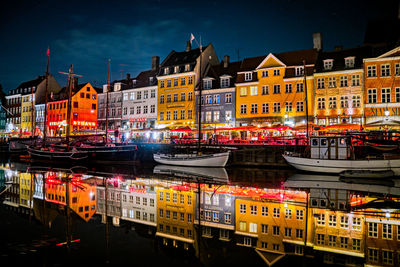 Illuminated buildings by canal in city at night