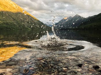 Water flowing through rocks in lake against sky