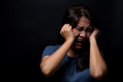 Scared young woman screaming while standing against black background