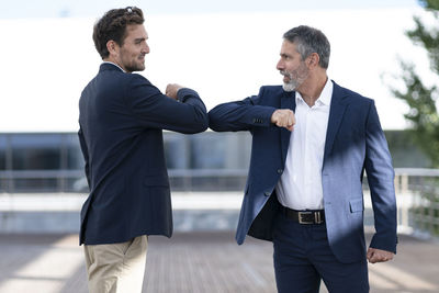 Entrepreneurs greeting with elbow bumps while standing at office terrace