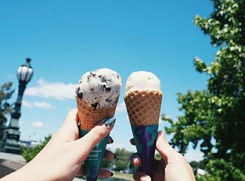 Cropped image of hand holding ice cream against sky