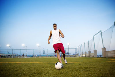Young man playing soccer on field against clear sky