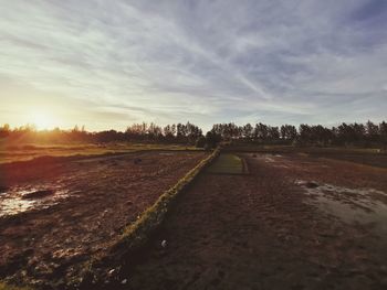 Road amidst field against sky during sunset