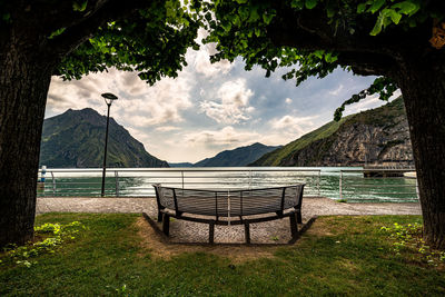 Empty bench by trees against sky