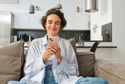 Young woman using mobile phone while sitting on bed at home